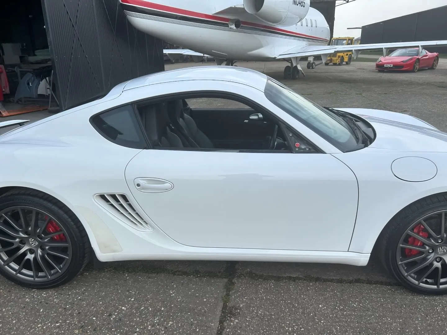 A white sports car parked in front of an airplane.