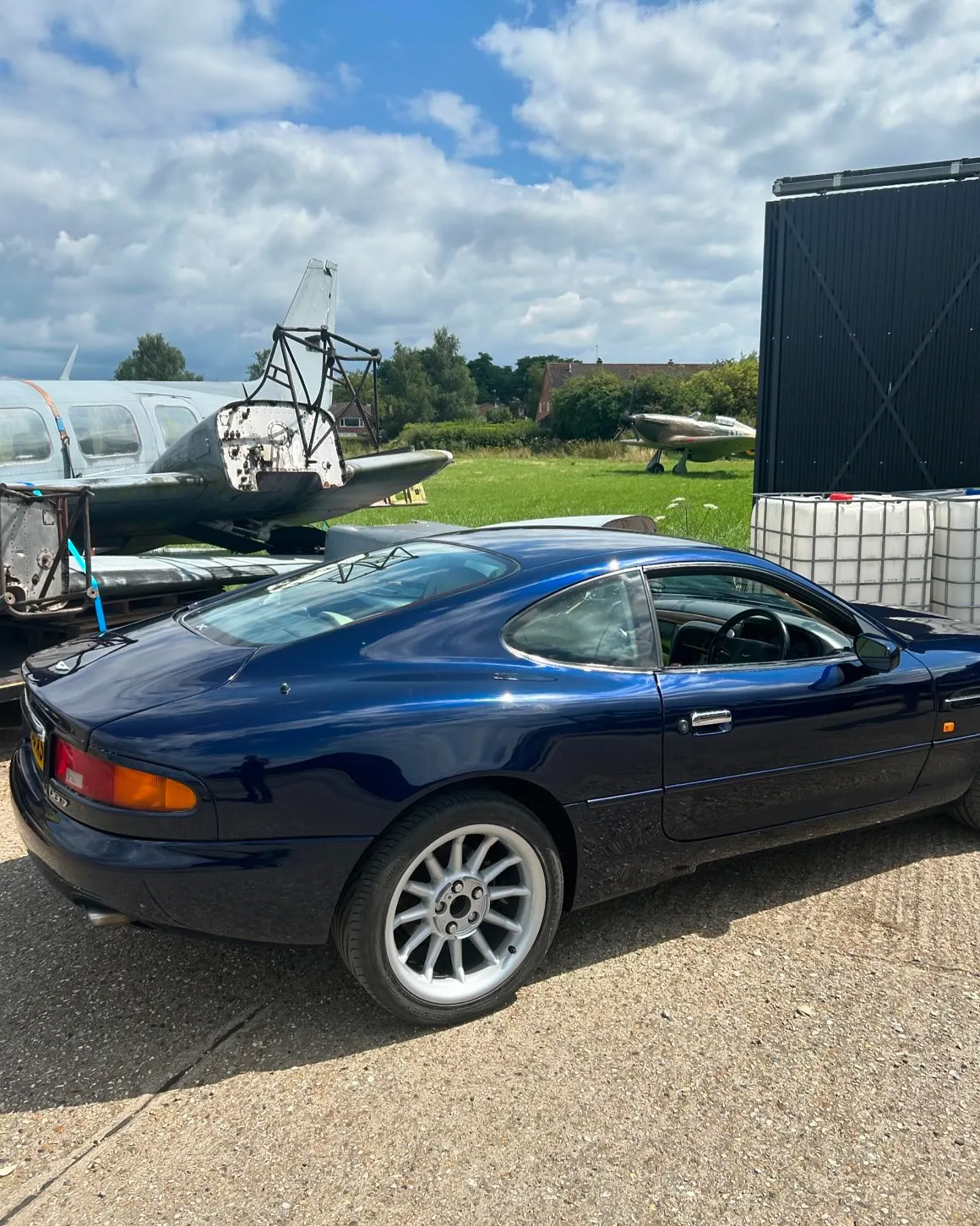 A blue sports car parked in front of an airplane.